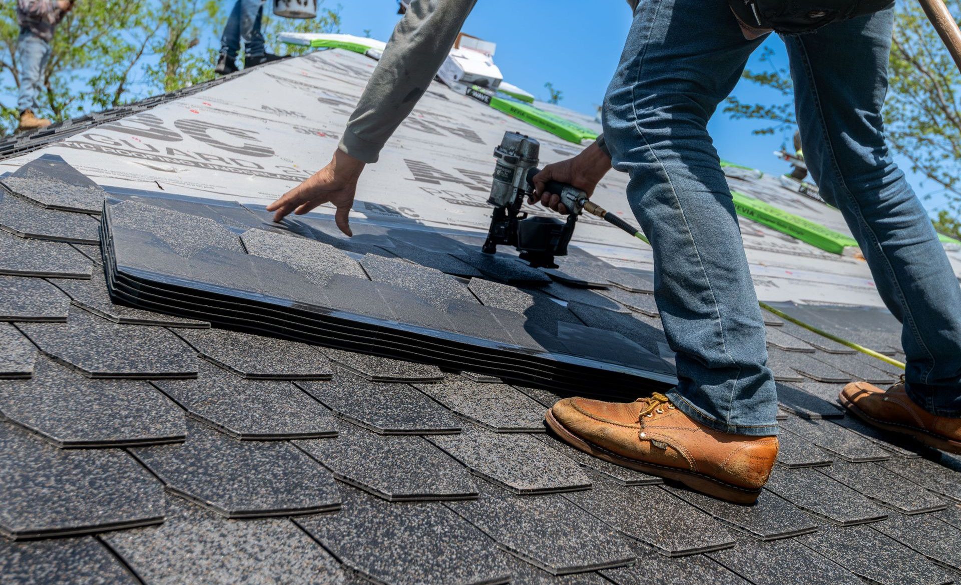 Roofer using nail gun for shingle installation on residential roof.